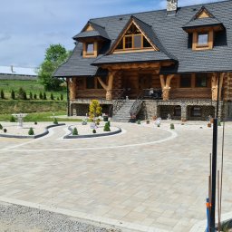 NOWBRUK - kompleksowe usługi brukarskie - Ułożona kostka brukowa przed domem w stylu góralskim. Widoczny ozdobny wzór z kostki, fontanna i zadbana zieleń. Całość tworzy elegancki i funkcjonalny podjazd.