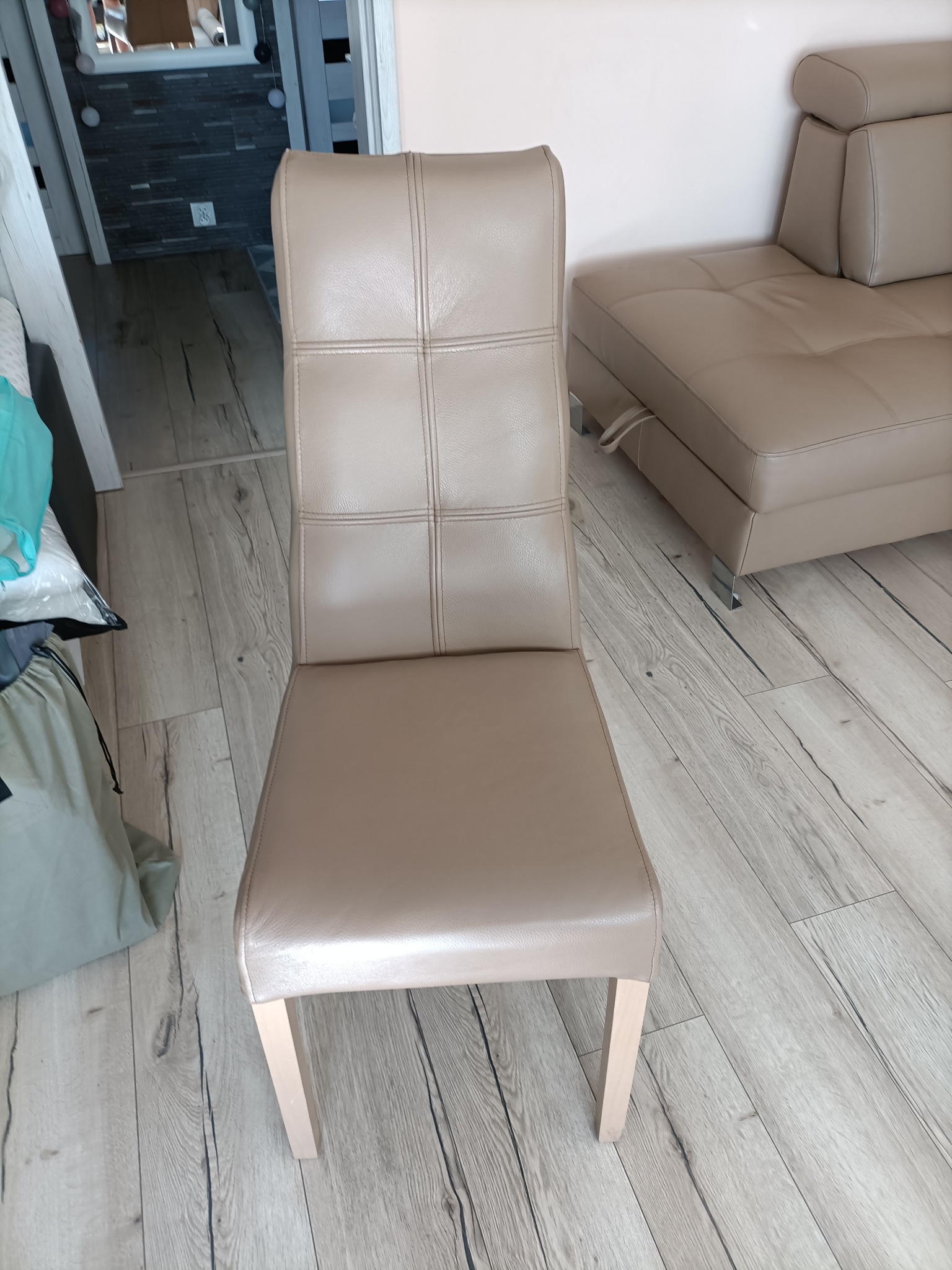 Beżowe krzesło z obiciem skórzanym i pikowanym oparciem, stojące na panelach podłogowych, obok beżowej sofy