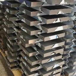 Stos metalowych, prostokątnych pojemników z zabezpieczeniem folią ochronną, ułożonych na palecie transportowej w hali produkcyjnej.