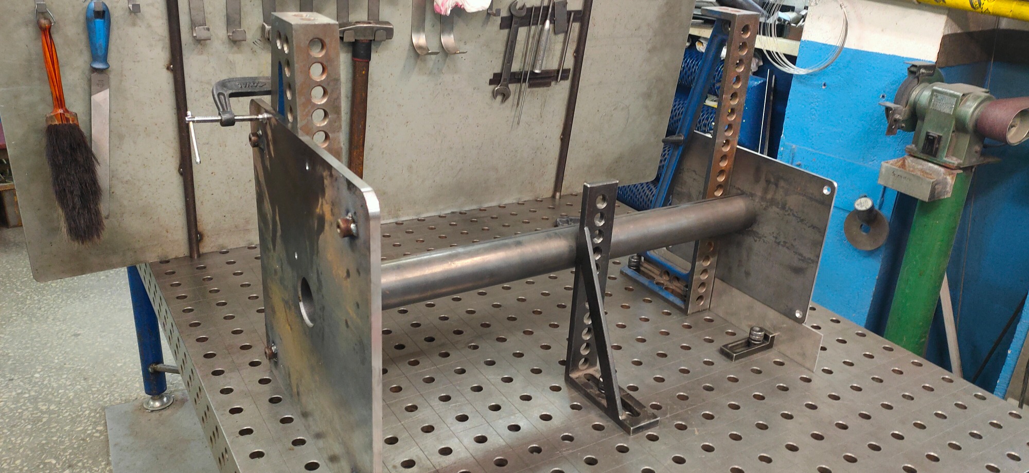 Metalowa rura spawana do dwóch płyt na perforowanym stole spawalniczym z narzędziami w tle.