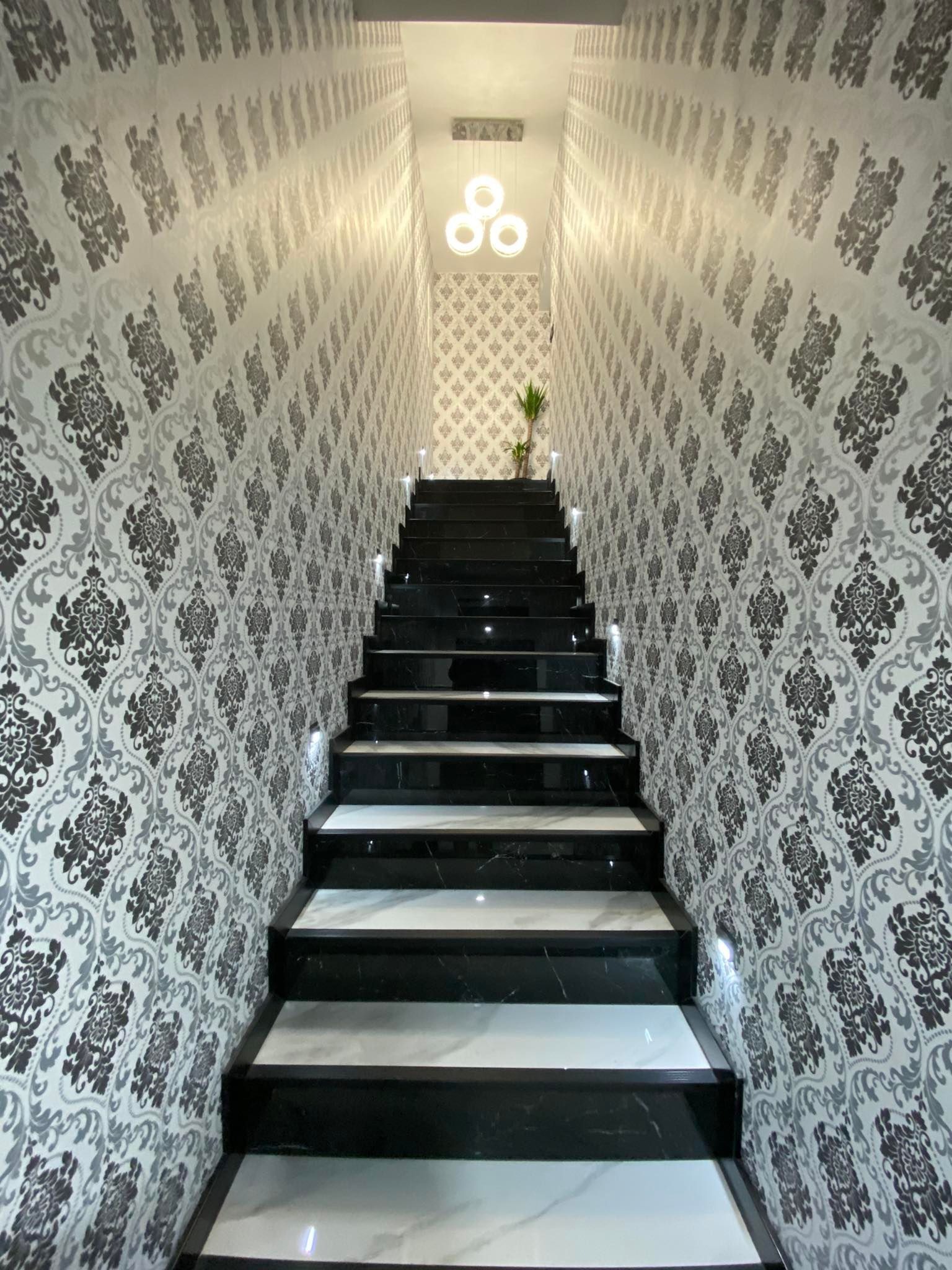 Schody z czarno-białego marmuru w Katowicach, oświetlone punktowymi lampami, prowadzące do góry, ściany wykończone tapetą w ornamenty.