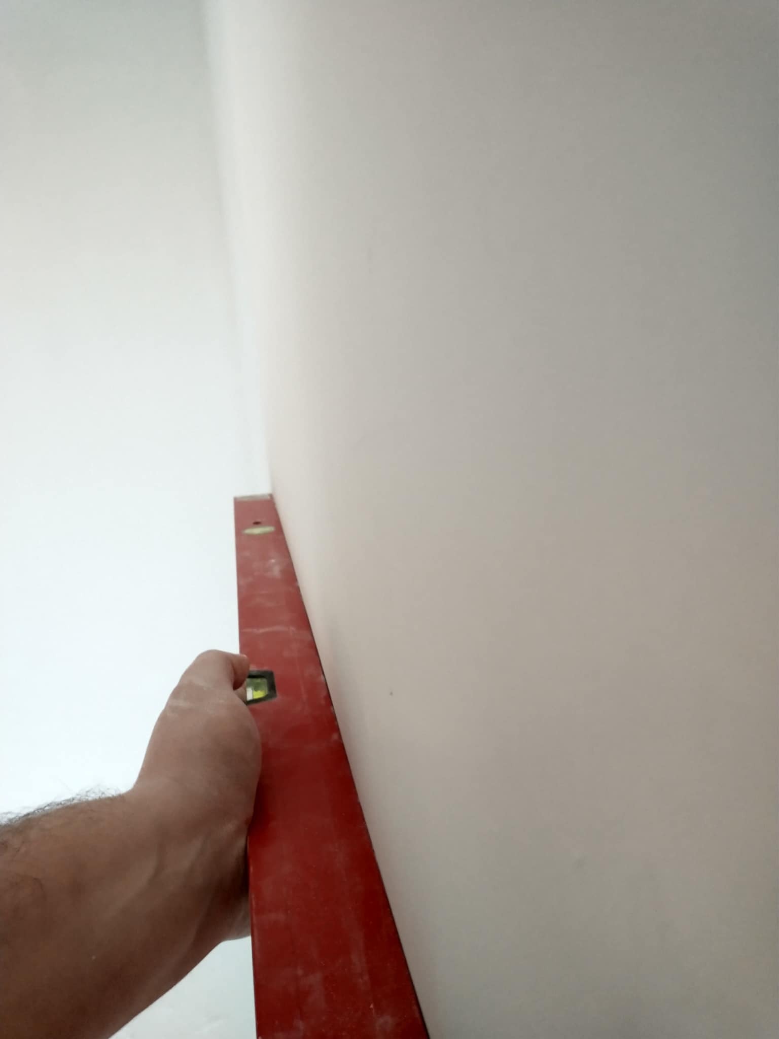 Czerwona poziomica przyłożona do świeżo pomalowanej, jasnej ściany w rogu pomieszczenia, sprawdzanie pionu