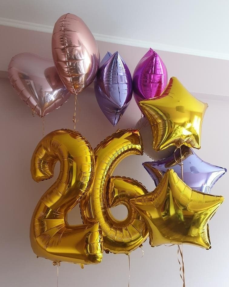 Kompozycja balonowa z foliowych balonów w kształcie cyfr '26', gwiazd i serc w odcieniach złota, różu i fioletu, zawieszona na tle jasnej ściany.