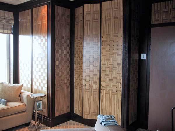 Wnętrze pokoju z zabudową szafy o dekoracyjnych frontach z wzorem plecionki, obok okno z roletą rzymską i sofa z małym stolikiem.