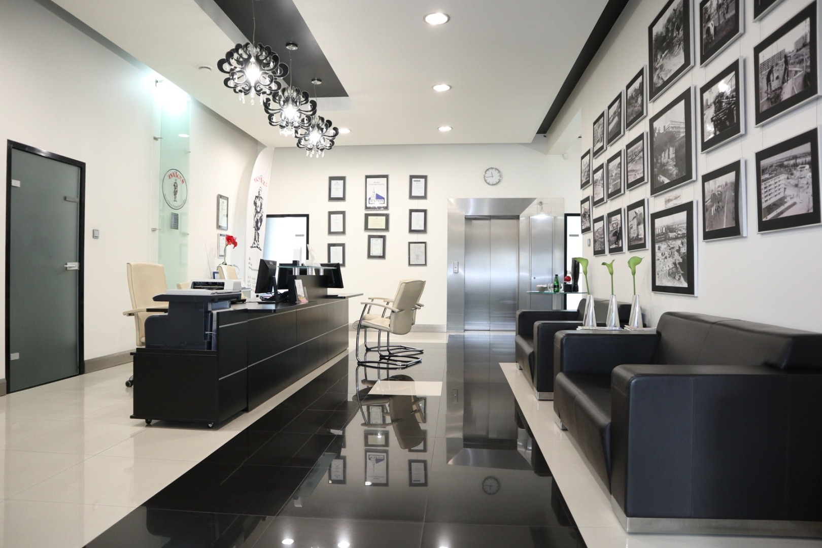 Eleganckie wnętrze biura agencji nieruchomości z recepcją, sofami dla klientów i ścianą ozdobioną czarno-białymi fotografiami.