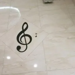 Jasne, marmurowe płytki podłogowe z inkrustowaną czarną nutą muzyczną w kształcie klucza wiolinowego i ósemki, narzędzia glazurnicze leżące przy ścianie.