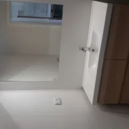 Nowoczesna łazienka z białymi płytkami, drewnianą szafką pod umywalką z białym blatem i minimalistycznym oświetleniem LED nad lustrem.