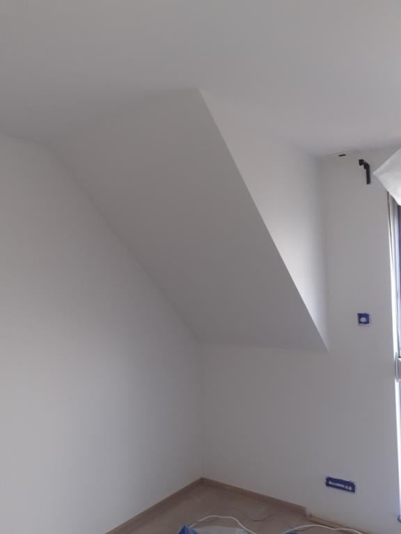 Pomalowane na biało poddasze ze skośnym sufitem i widocznymi puszkami elektrycznymi, świeżo po malowaniu.