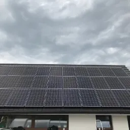 Panele słoneczne na dachu domu jednorodzinnego z brązową dachówką, widok na pochmurne niebo.