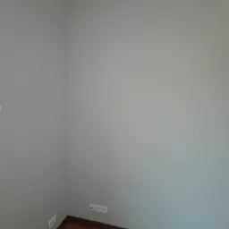 Świeżo pomalowane na szaro ściany w rogu pokoju w Tarnowie, widoczne gniazdka elektryczne i drewniana podłoga.