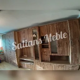 Zabudowa meblowa z drewna o widocznej strukturze, obejmująca szafy z pełnymi frontami oraz witryny z przeszkleniami, widok z dołu, w tle okno z książkami