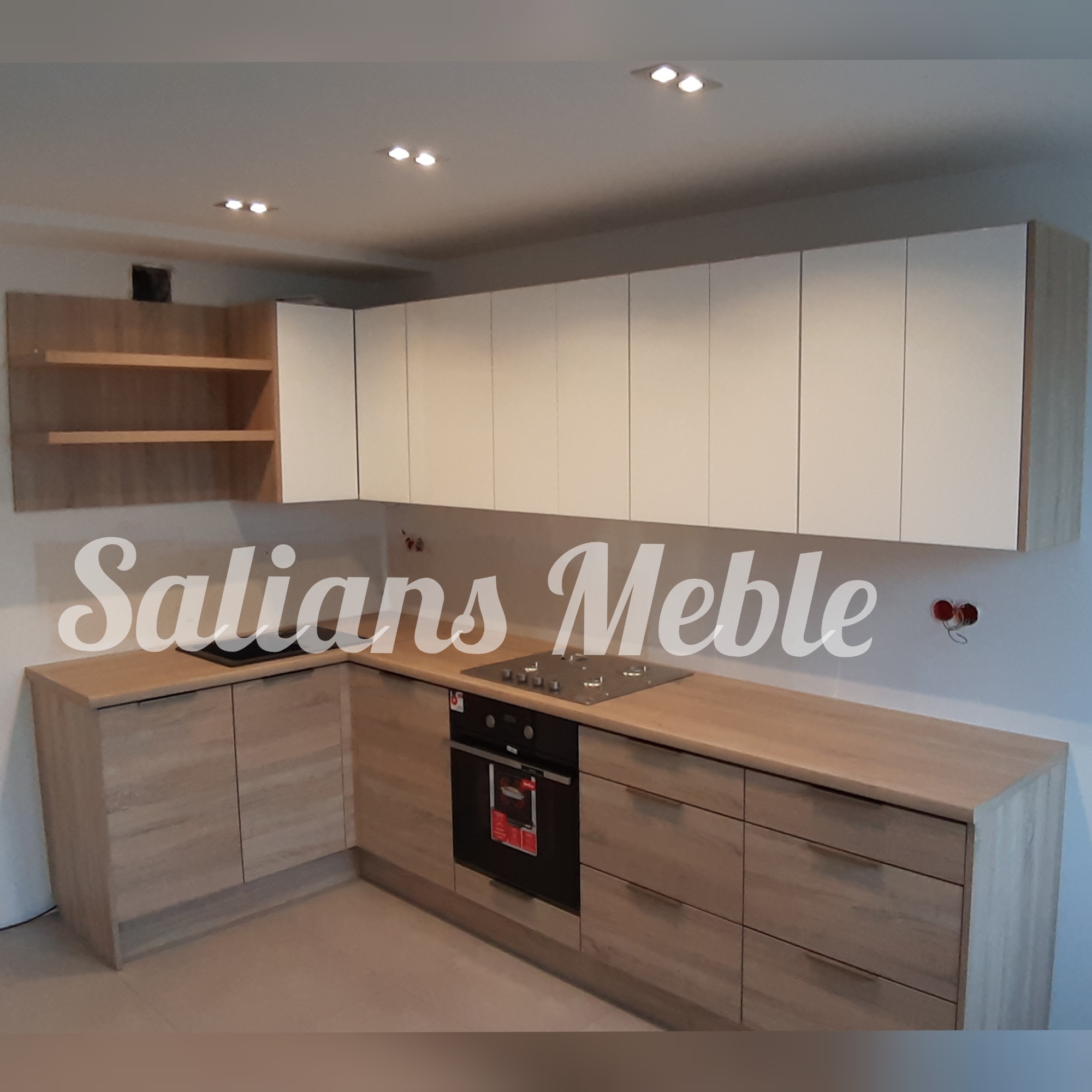 Nowoczesna kuchnia z jasnymi drewnianymi szafkami dolnymi i białymi górnymi, z piekarnikiem i płytą gazową w zabudowie, widoczne gniazdka elektryczne bez osprzętu.