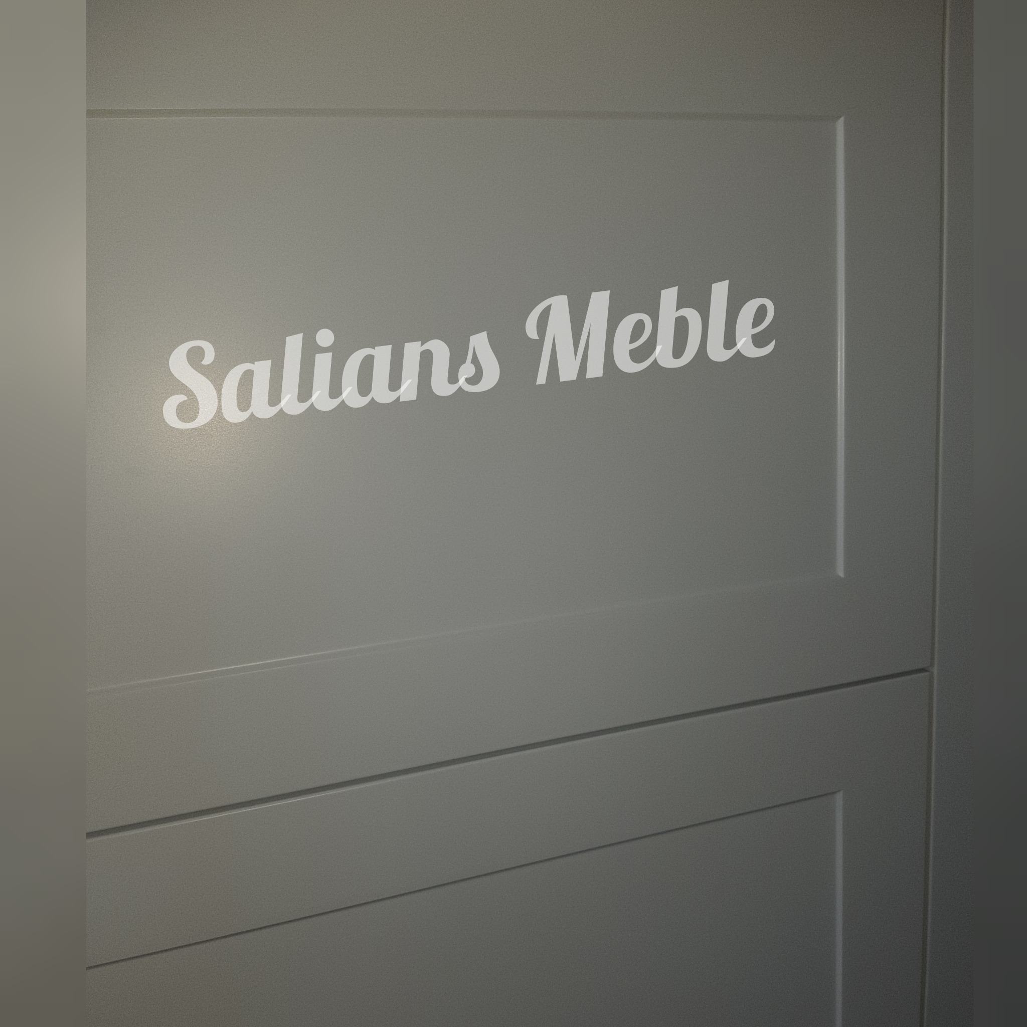 Fragment szarej szafy z frezowanymi frontami i napisem 'Salians Meble' w białej czcionce.