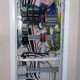 Smart Home Leszno - Inteligentny Dom IGVEL - Głogów, Rawicz, Gostyń, Kościan, Śrem - Rozdzielnia elektryczna w białej obudowie, widoczne przewody z oznaczeniami LED, moduły sterujące Ampio i zabezpieczenia. Instalacja w ścianie, schludne ułożenie kabli.