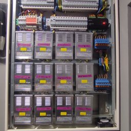 Smart Home Leszno - Inteligentny Dom IGVEL - Głogów, Rawicz, Gostyń, Kościan, Śrem - Rozdzielnia elektryczna w obudowie, z licznymi modułami i przewodami, zasilacze z etykietami 'SALA', 'BAR', 'VIP', zamontowana na szarej ścianie.