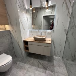 B&B - Nowoczesna łazienka z marmurowymi płytkami, beżową umywalką nablatową i wiszącą toaletą. Widoczne oświetlenie punktowe i fragment kabiny prysznicowej.