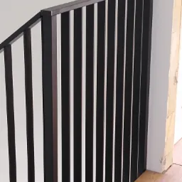 Nowoczesna, czarna balustrada schodowa z pionowymi szczebelkami, zamontowana przy białej ścianie i drewnianej podłodze.