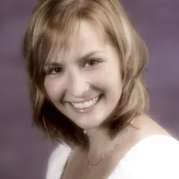 Portret uśmiechniętej młodej kobiety z blond włosami, na fioletowym tle, w białej bluzce i z delikatnym naszyjnikiem.