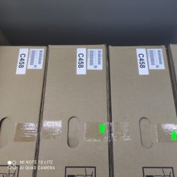 Copix Sp z o.o. - Kilkanaście zapakowanych w kartony kserokopiarek w magazynie w Warszawie, widoczne etykiety z kodami C458 i fragmenty taśmy zabezpieczającej.