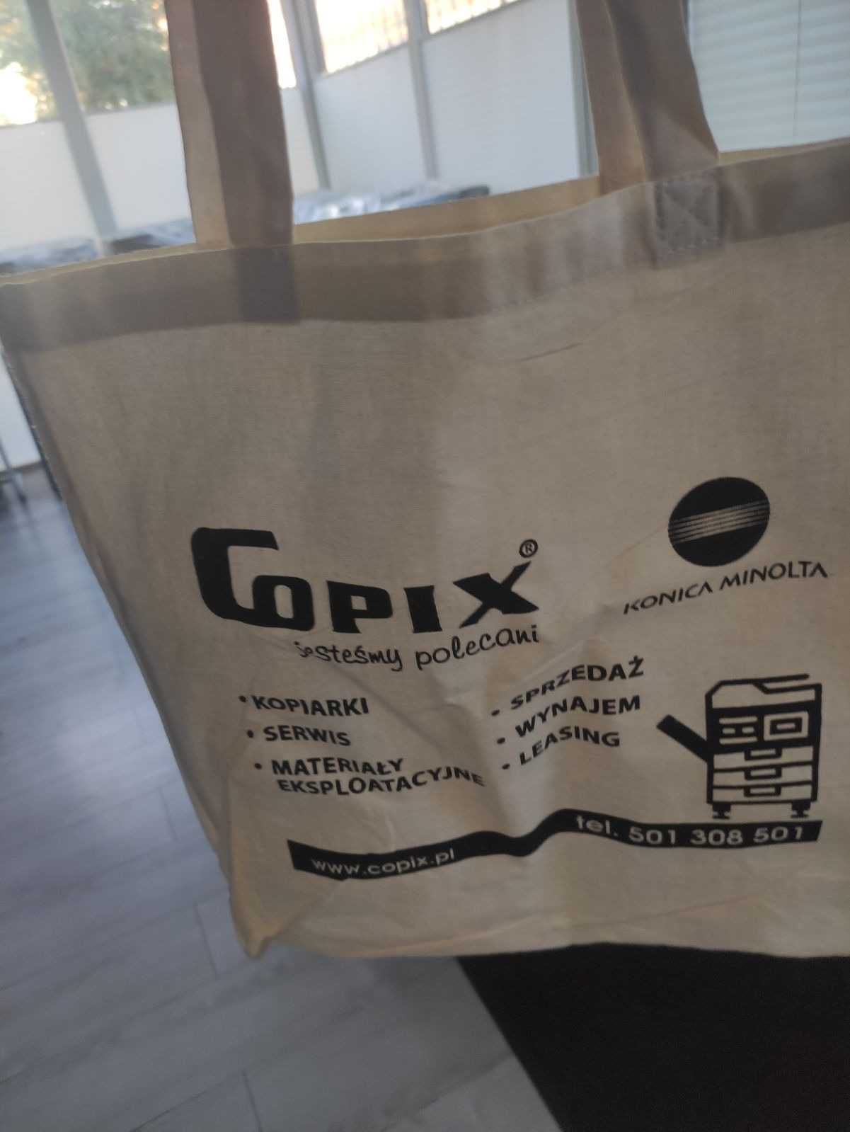 Eko-torba z nadrukowanym logo firmy Copix i Konica Minolta, oferującej sprzedaż, wynajem, leasing, serwis i materiały eksploatacyjne do kserokopiarek, z podanym numerem telefonu i adresem strony...