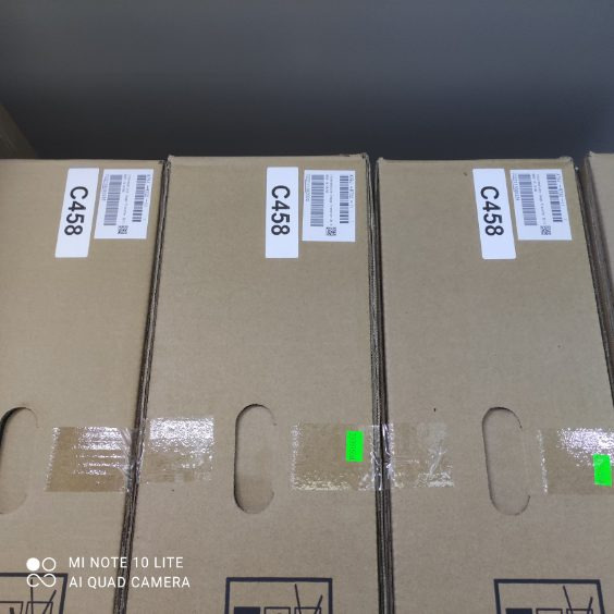 Kilkanaście zapakowanych w kartony kserokopiarek w magazynie w Warszawie, widoczne etykiety z kodami C458 i fragmenty taśmy zabezpieczającej.