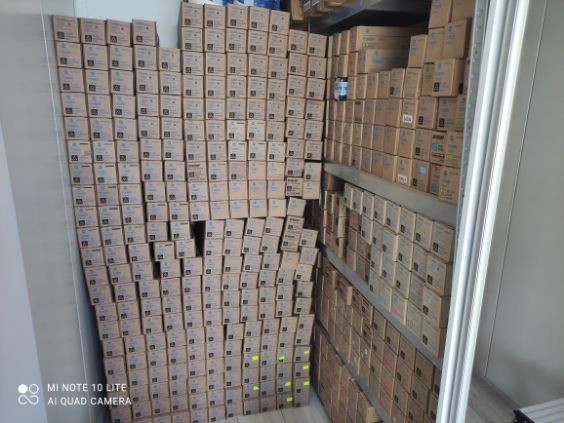 Magazyn wypełniony po brzegi kartonami z tonerami do drukarek i kserokopiarek, ułożonymi na półkach i bezpośrednio na podłodze.