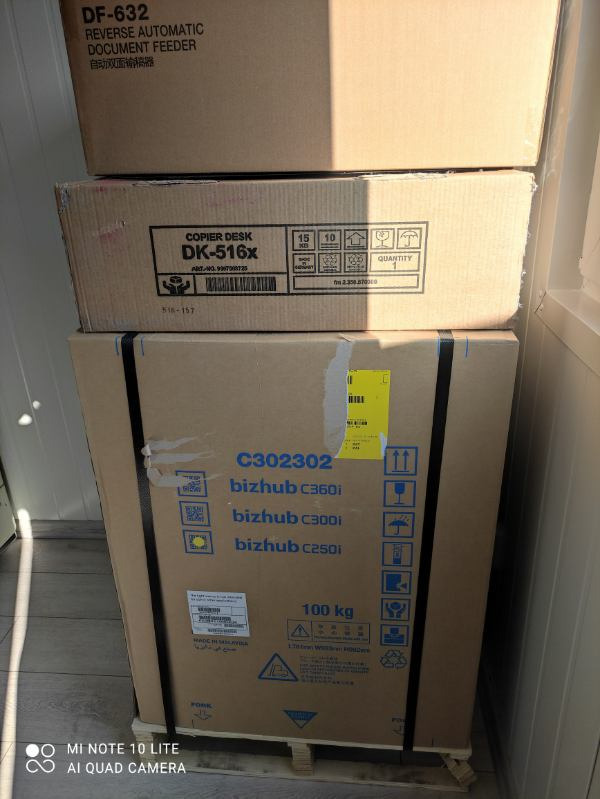 Stos kartonowych pudeł z oznaczeniami modeli kserokopiarek Bizhub C360i, C300i i C250i oraz modułu DF-632, umieszczonych na drewnianej palecie.