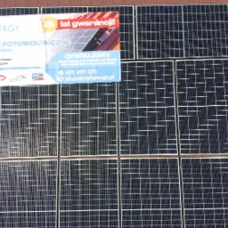 Instalacja fotowoltaiczna na dachu w miejscowości Ruda-Bugaj, z widocznym banerem reklamowym firmy oferującej 25 lat gwarancji, darmowe ogrzewanie słoneczne i folie grzewcze na podczerwień.