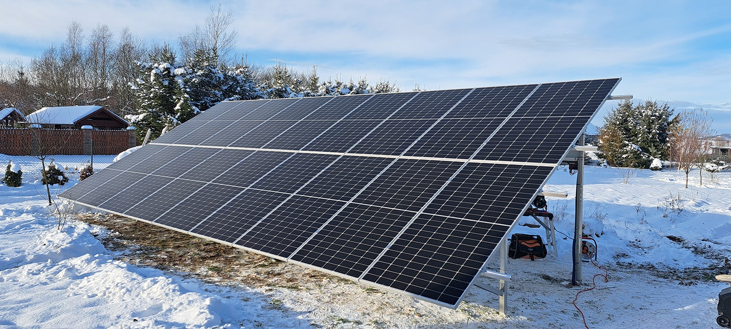Panel słoneczny na tle zimowego krajobrazu. Widoczne narzędzia i skrzynka narzędziowa, sugerujące niedawny montaż. Błękitne niebo i ośnieżone drzewa w tle.
