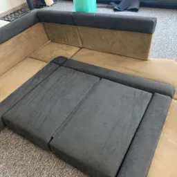 Narożnik modułowy z elementami w kolorze beżowym i grafitowym, widoczne szwy i łączenia poszczególnych modułów, na podłodze szary dywan.