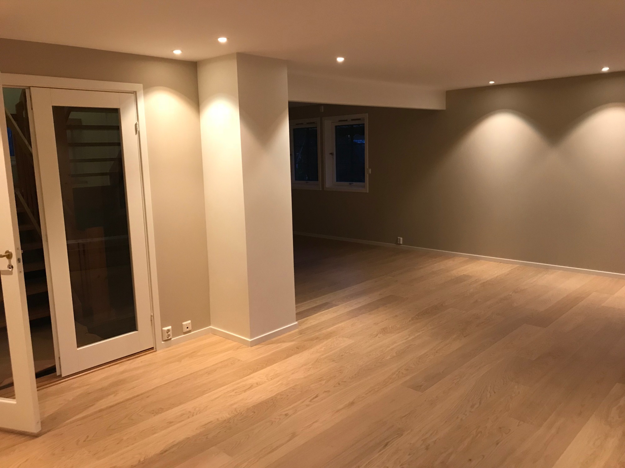 Jasne panele podłogowe z widocznym usłojeniem w nowo wyremontowanym salonie z beżowymi ścianami, białymi drzwiami z przeszkleniami i punktowym oświetleniem.