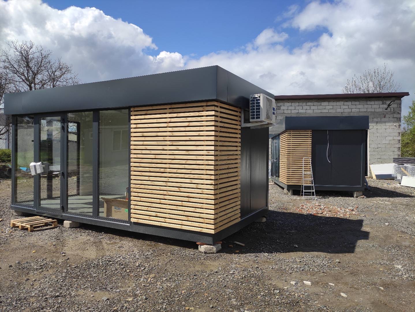 Nowoczesny pawilon z płyt warstwowych z drewnianą elewacją i klimatyzacją, widok z zewnątrz na tle pochmurnego nieba i budynku z cegły.