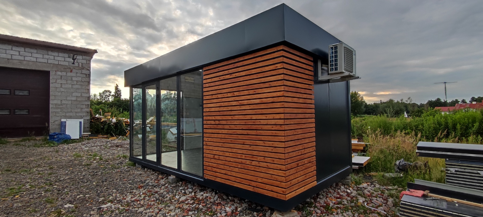 Nowoczesny, modułowy pawilon z przeszkleniami i drewnianą elewacją, klimatyzator na bocznej ścianie, widok z zewnątrz.