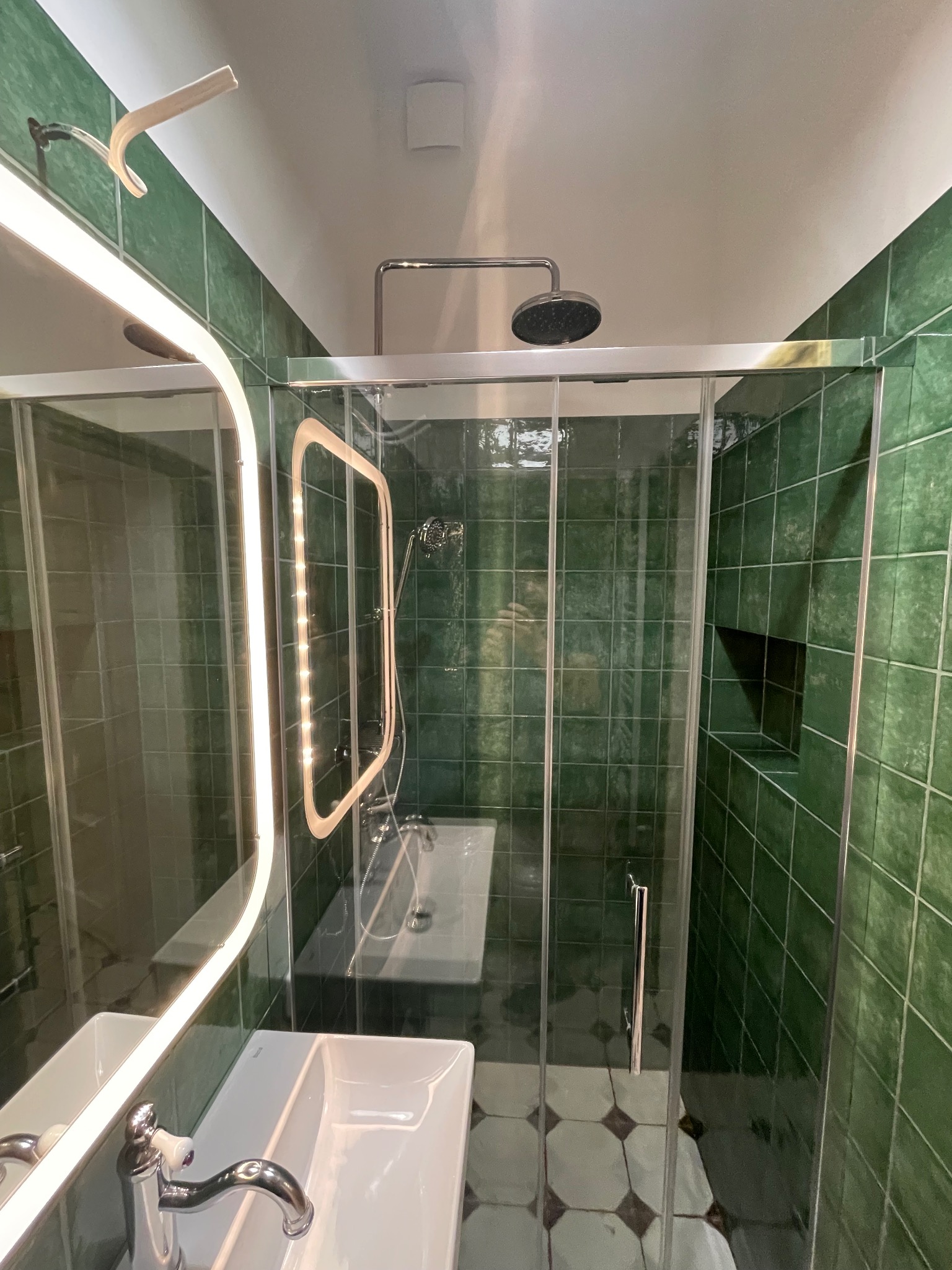 Nowoczesna łazienka z zielonymi płytkami, kabiną prysznicową typu walk-in i podświetlanym lustrem. Umywalka z chromowaną baterią. Widok z góry.