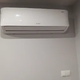 Biała jednostka klimatyzacji marki Rotenso zamontowana na szarej ścianie w Harasiukach, widoczne włączniki światła na dole kadru.