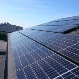 Panel słoneczny na dachu domu jednorodzinnego, widok z góry, błękitne niebo w tle.