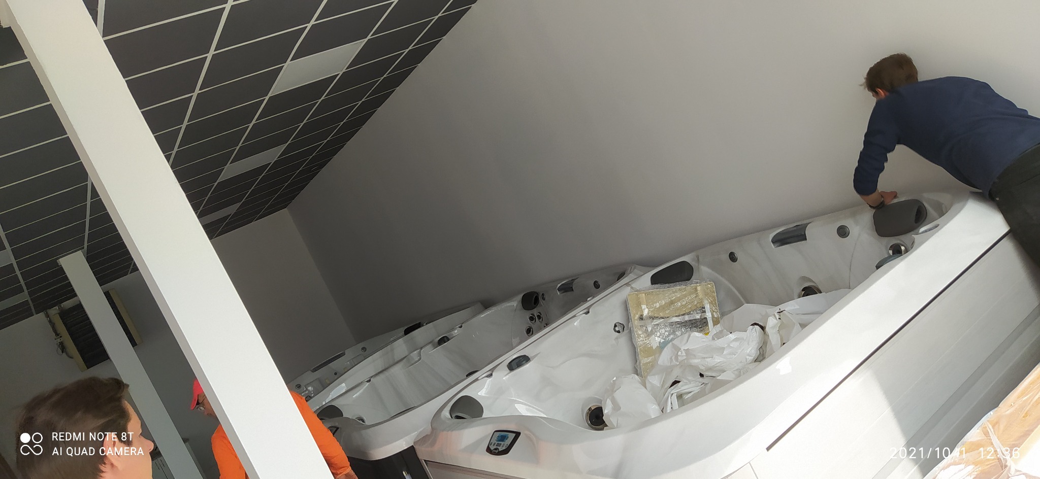 Montaż lub ustawianie białych wanien spa w pomieszczeniu z szarą kasetonową podwieszaną sufitem. Widoczni pracownicy w trakcie pracy.