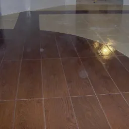 Ukończona podłoga z płytek imitujących drewno w kształcie łuku, połączona z jasnymi płytkami kwadratowymi, obok kolumna wyłożona mozaiką.