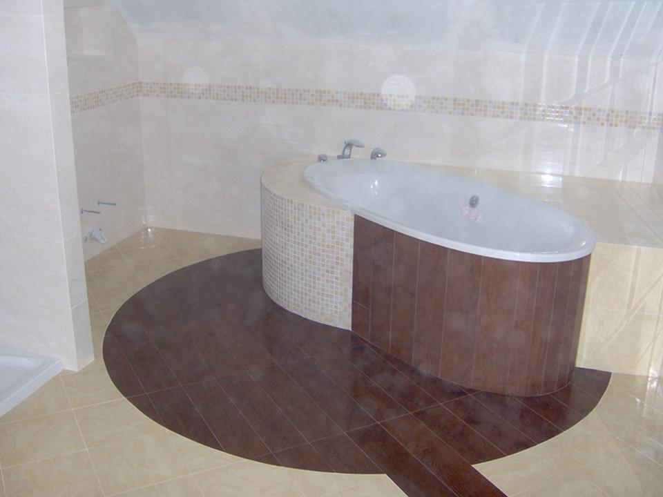 Nowoczesna łazienka z owalną wanną obudowaną mozaiką i ciemnobrązowymi panelami, podłoga z jasnych i ciemnych płytek ułożonych w okrąg