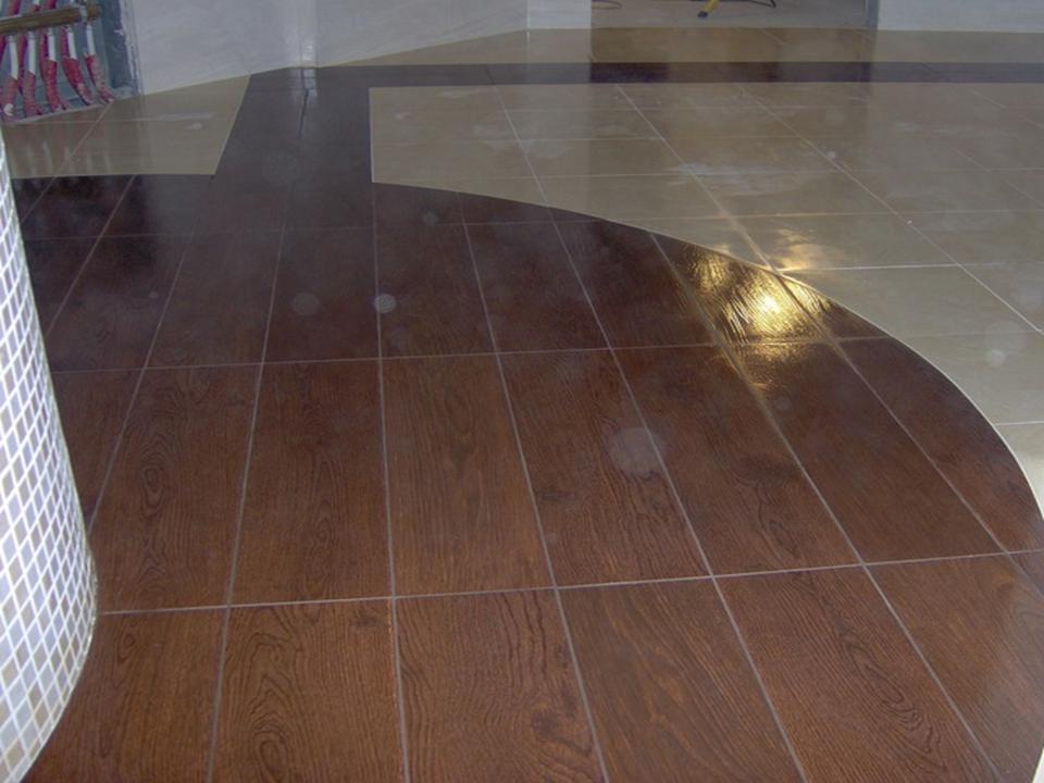 Ukończona podłoga z płytek imitujących drewno w kształcie łuku, połączona z jasnymi płytkami kwadratowymi, obok kolumna wyłożona mozaiką.