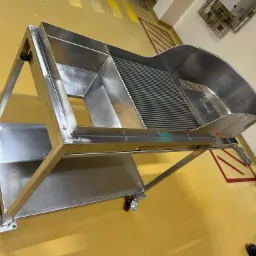 Stalowa konstrukcja na kółkach z trzema różnymi powierzchniami: pełną, kratową i siatkową, przeznaczona prawdopodobnie do sortowania lub przesiewania.