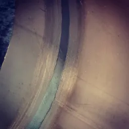 Zbliżenie na spoinę na metalowej powierzchni z widocznymi śladami obróbki.