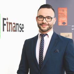 Wojciech Jastrzębski Fotografia Produktowa - Portret uśmiechniętego mężczyzny w okularach i granatowym garniturze z poszetką, na tle biura firmy finansowej w Łodzi z logo i hasłami reklamowymi.