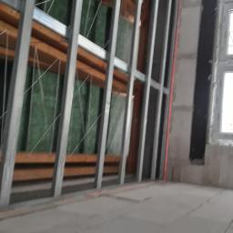 Marbud - Konstrukcja z profili stalowych do montażu płyt gipsowo-kartonowych, widoczna izolacja z wełny mineralnej oraz drewniane elementy wzmacniające, surowy stan pomieszczenia z oknem.