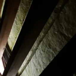 Skośny widok na krokwie dachowe z widoczną izolacją z wełny mineralnej, przymocowaną drutem.