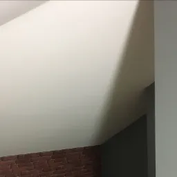 Poddasze po remoncie: skośny sufit pomalowany na biało, fragment ściany wykończony czerwoną cegłą, sąsiadująca ściana w kolorze szarym.