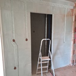 M&M Electro - Surowy stan ścian z wyfrezowanymi bruzdami pod przewody elektryczne, widoczne puszki instalacyjne, drabina aluminiowa, kable na podłodze.