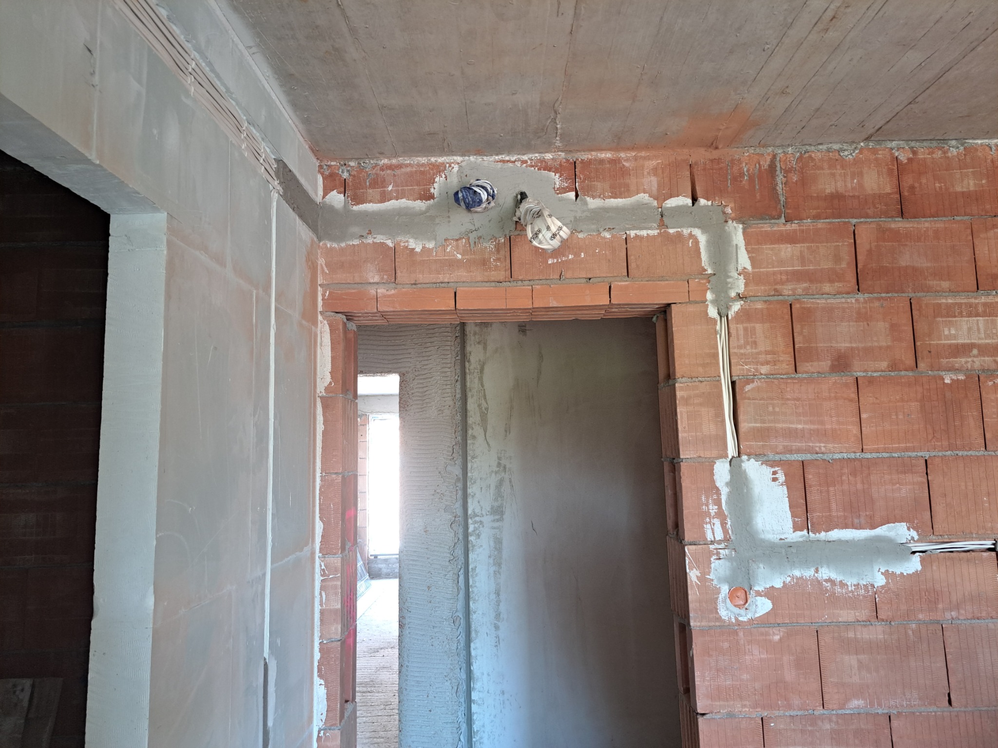 Wewnętrzne ściany budynku w trakcie budowy, widoczne kable elektryczne w bruzdach zalane zaprawą, puszki elektryczne zabezpieczone folią.