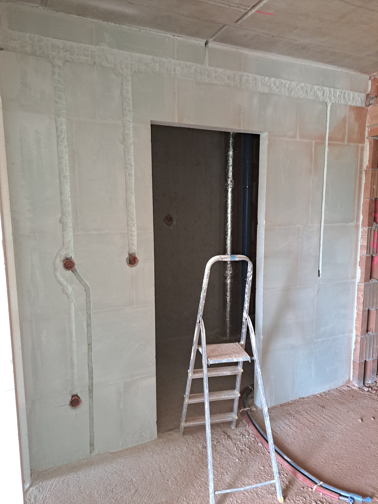 Surowy stan ścian z wyfrezowanymi bruzdami pod przewody elektryczne, widoczne puszki instalacyjne, drabina aluminiowa, kable na podłodze.