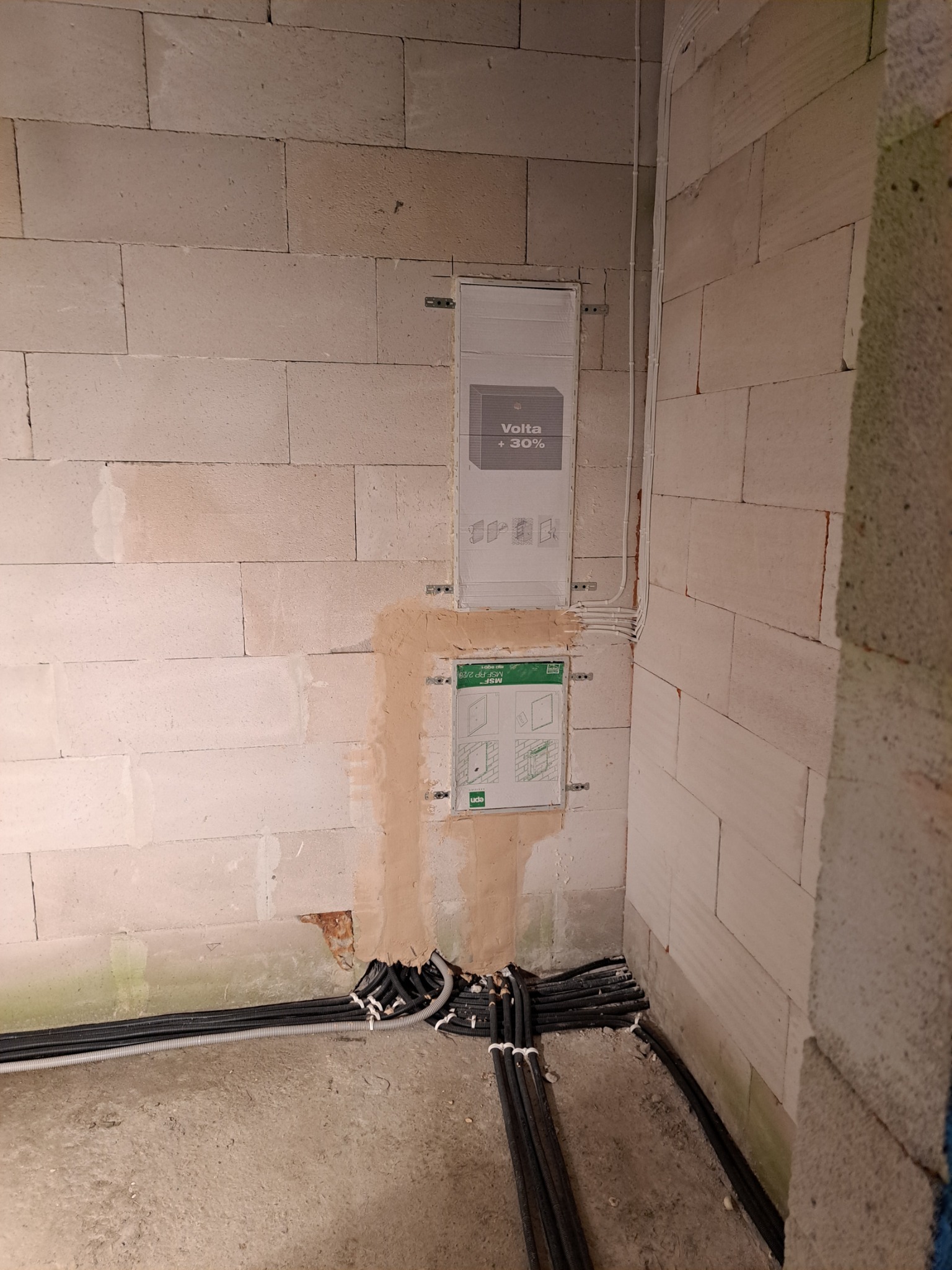 Wewnętrzna instalacja elektryczna w trakcie montażu: kable w czarnych peszlach wchodzą do puszki podtynkowej w surowej ścianie z betonu komórkowego, widoczne oznaczenia producenta Volta +30%.